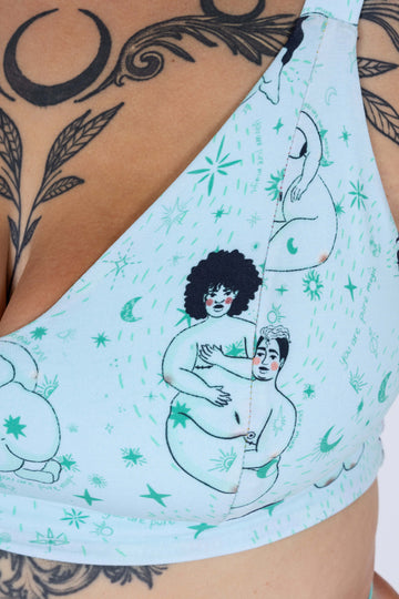 Closeup of Tattooed model wearing Wilde Mode x Fat Lemon Mint Comfort Briefs and Comfort Bra. The print is of a naked lady with amongst stars. The waist and leg bands are a teal blue mint colour.