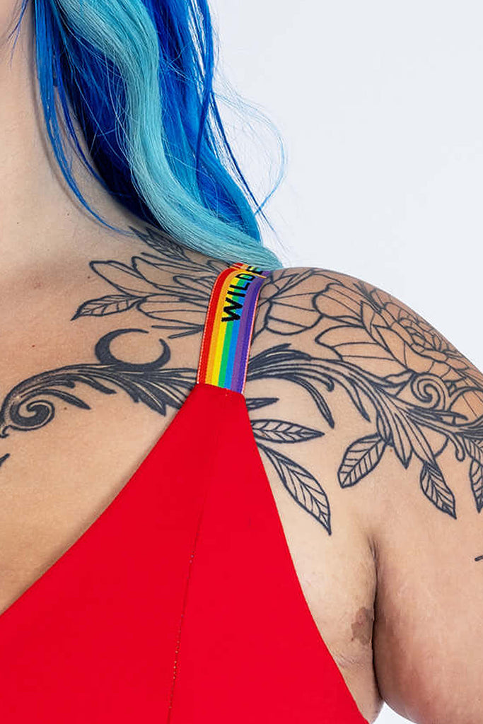 Close up of Wilde Mode Adjustable Slider Bra Straps in rainbow, shown on a model. The straps are rainbow striped with 'Wilde Mode' written across in black. 