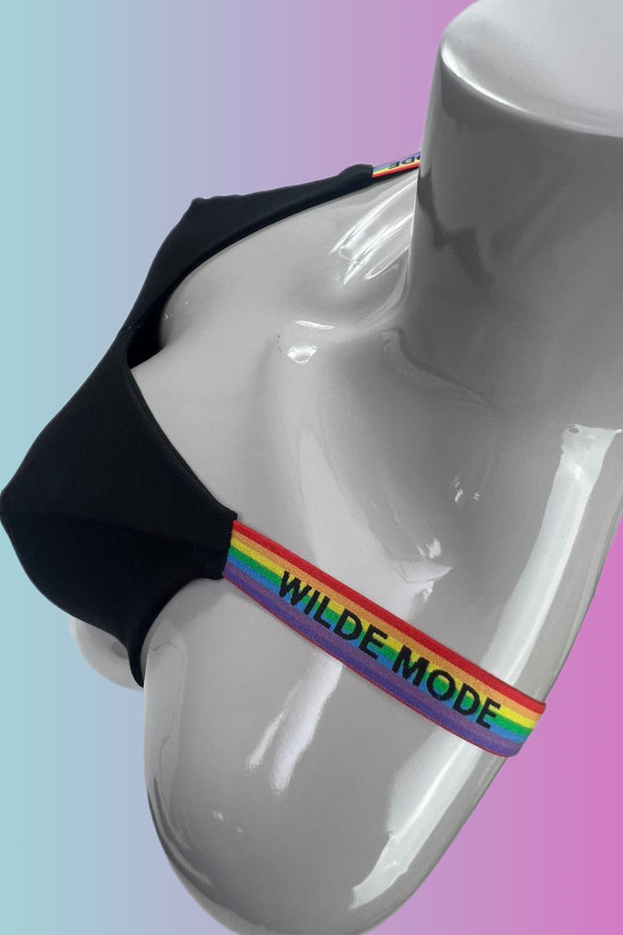 Close up of Wilde Mode Adjustable Slider Bra Straps in rainbow, shown on a mannequin. The straps are rainbow striped with 'Wilde Mode' written across in black.