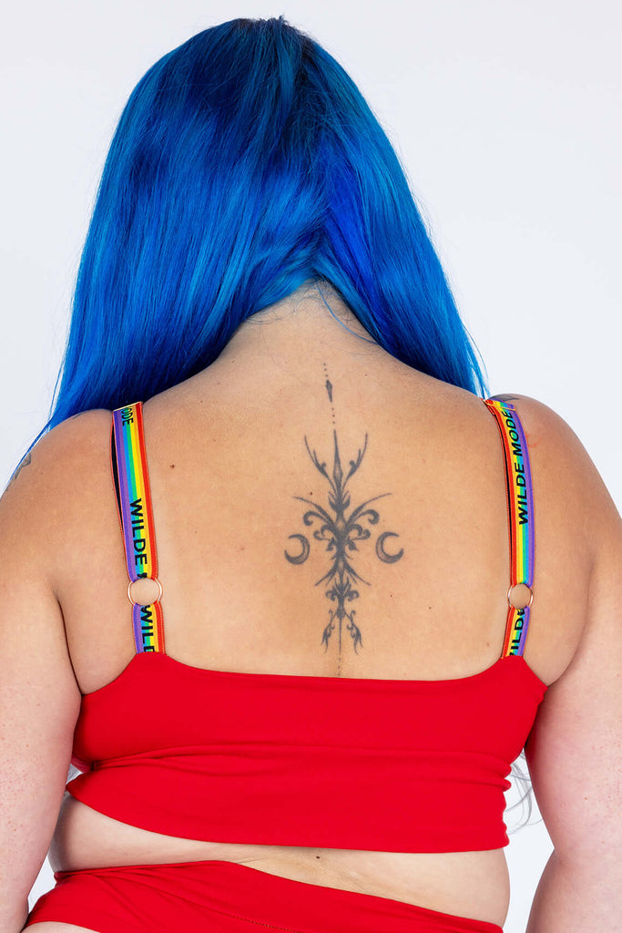 Model wearing Red Comfort Bra with Wilde Mode Rainbow Adjustable Slider Bra Straps. Model is standing with their back to the camera to show the straps which are rainbow striped and have 'Wilde Mode" written across them in black. They have O rings on the back of them for adjusting. 