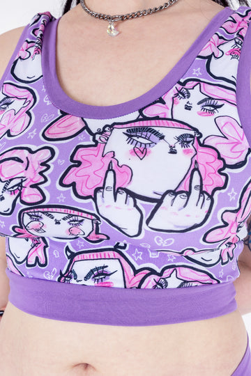 Tattooed model wearing Wilde Mode x Twinkle and Gloom Lilac Angry Feminist Comfort Top. The print is of angry pink cartoon faces holding up middle fingers on a purple background. The band is also purple.