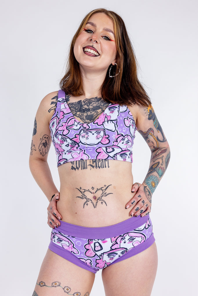 Tattooed model wearing Wilde Mode x Twinkle and Gloom Lilac Angry Feminist Comfort Briefs and Bra. The print is of angry pink cartoon faces holding up middle fingers on a purple background. The band on the brief is also purple.
