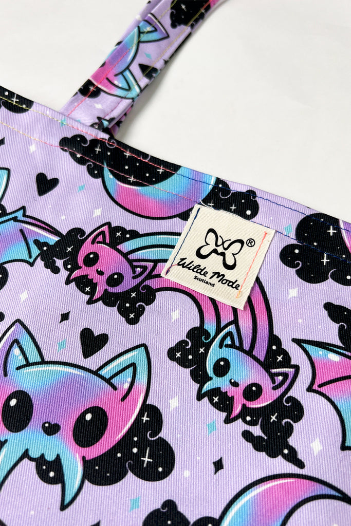 Close up of 100% Organic Cotton Cyber Bats Tote Bag. A pastel purple tote bag with cute bat design with rainbows, clouds and love hearts with Wilde Mode logo on label.