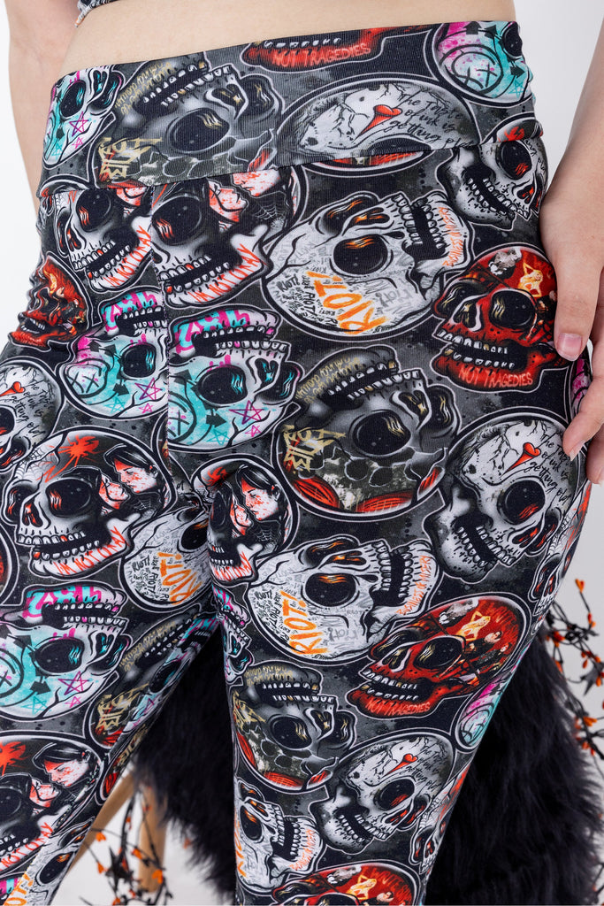 Close up shot of Emo Skulls active loungewear leggings are black grey with red blue orange emo alternative music bands print. Worn by an alternative model with brown and pink hair in bunches, with heavy winged eyeliner, posing with hand on hip. Made sustainably in the UK by Wilde Mode.