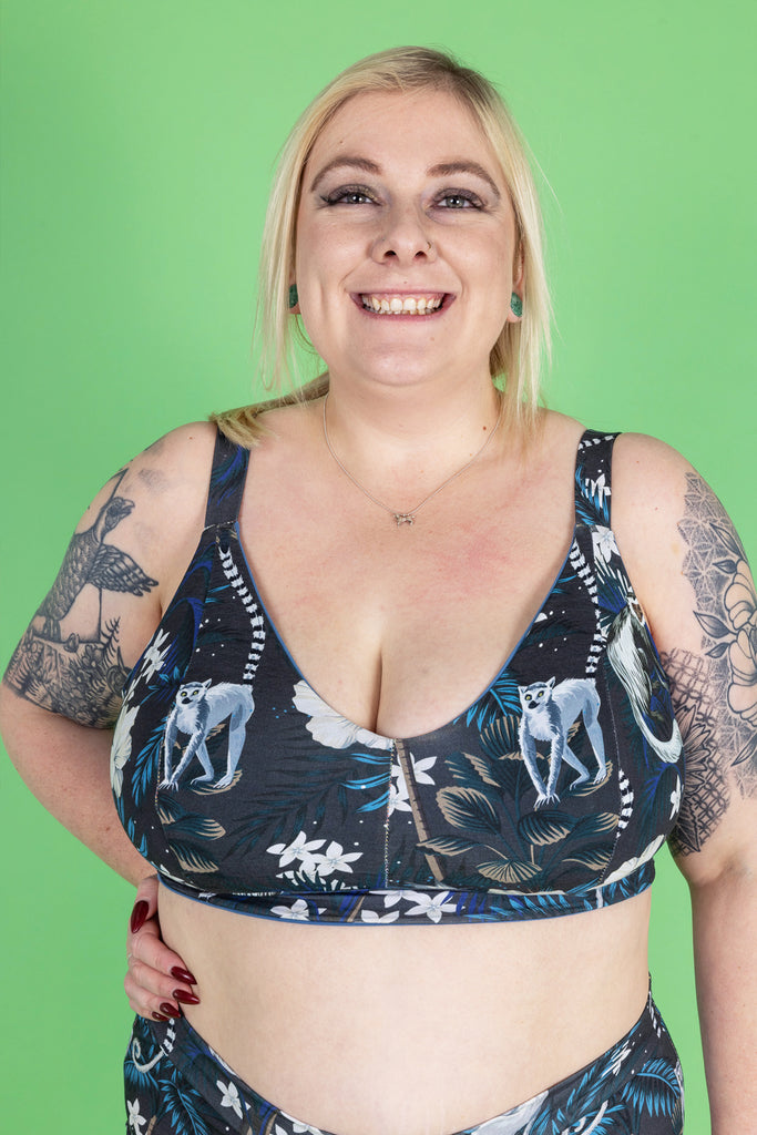 Alicia is a smiley blonde curvy female with tattoos. Her hair is loosely tied back and she is wearing a matching underwear set featuring monkeys and florals on a dark navy background.