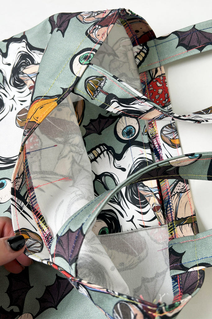 A mint green coloured tote bag with creepy mushroom print with skulls and eyeballs with bat wings