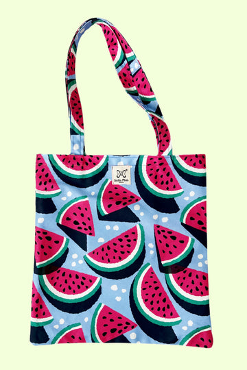 a blue tote bag with watermelon slices print all over. Shown on a pale yellow background