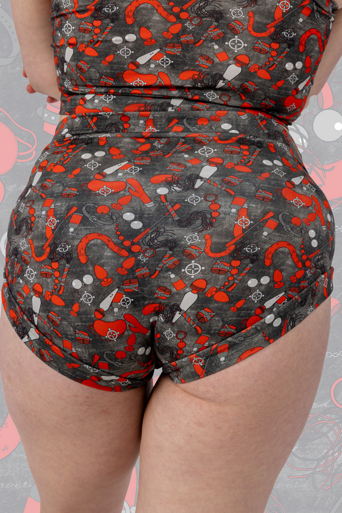 Model is wearing What’s Your Kink? 18+ Ultra Naughty Comfort Briefs paired with comfort top. The briefs are grey with various red sex toys all over. Model is posing with bum to camera.